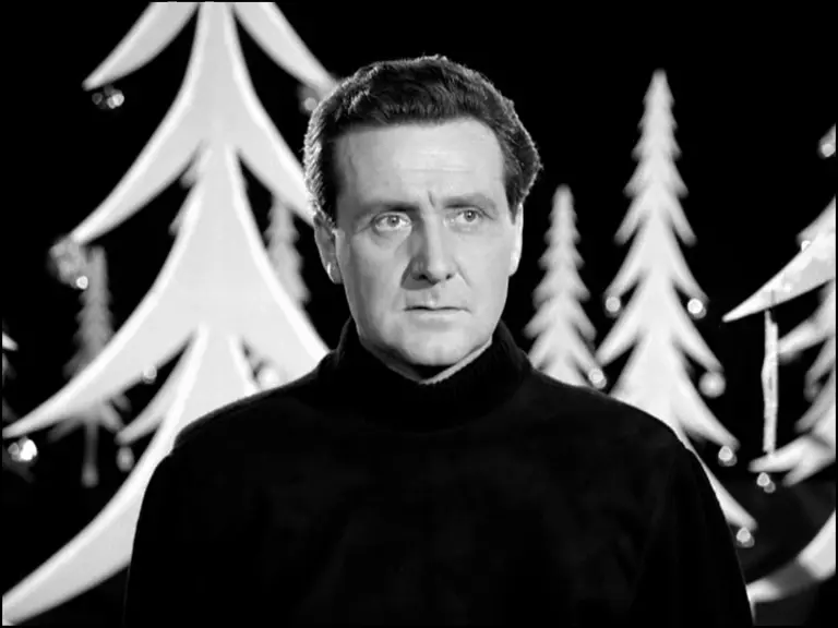 Patrick Macnee surrounded by cutout Christmas trees