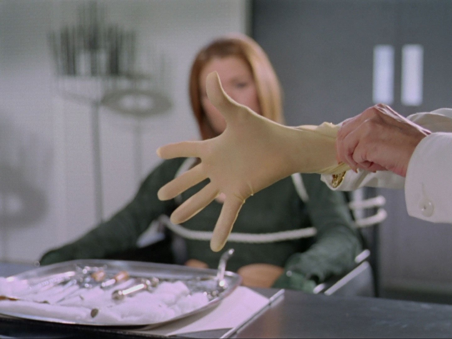 A latex-gloved hand near some surgical instruments