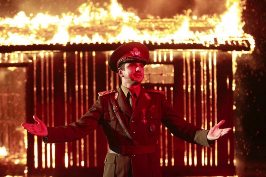 An army officer in front of a burning building