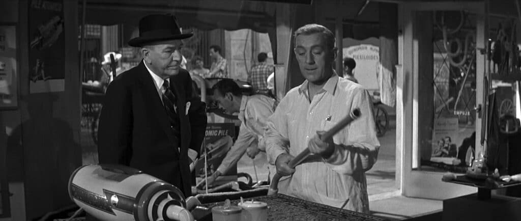 Hawthorne looks on as Wormold demonstrates a vacuum cleaner
