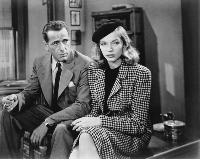 Boagart and Bacall sit on a desk