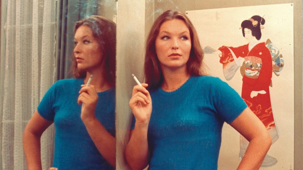 Juliette stands by a mirror smoking