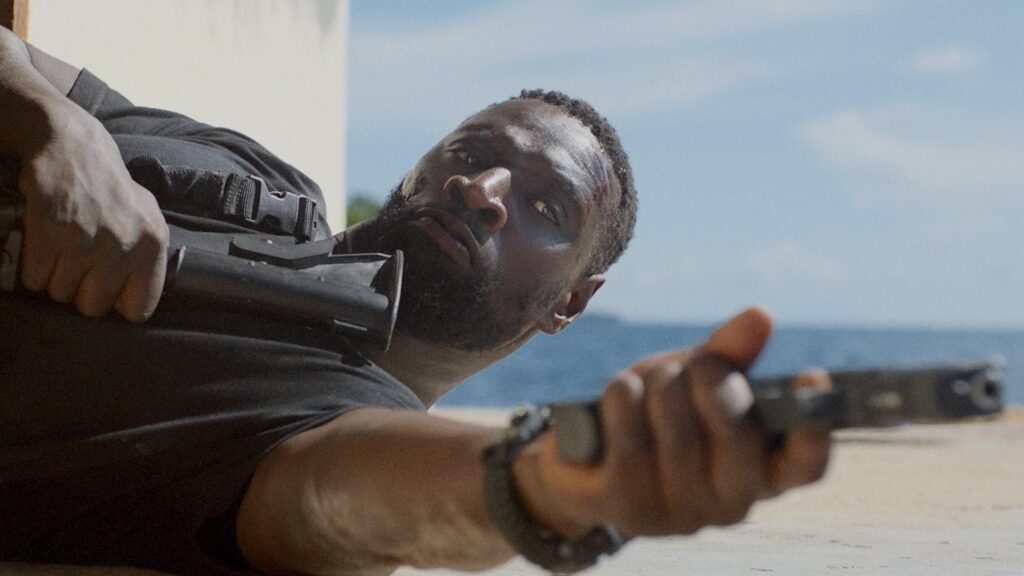 Omar Sy points a gun while lying on the ground