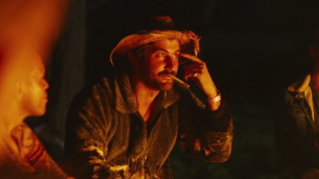 Dylan smokes a cigarette by the camp fire