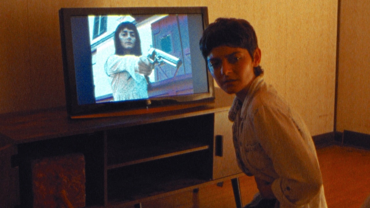 Frankie in front of a TV showing a woman aiming a gun