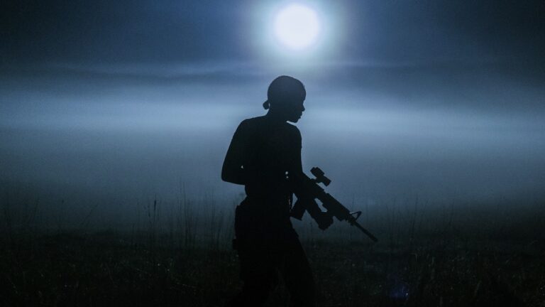 A silhouetted figure with an assult rifle