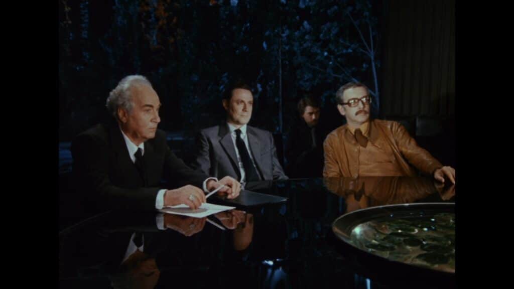 Three men sit around a table discussing the crisis