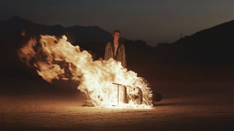 Rene stands behind a man burning to death tied to a chair