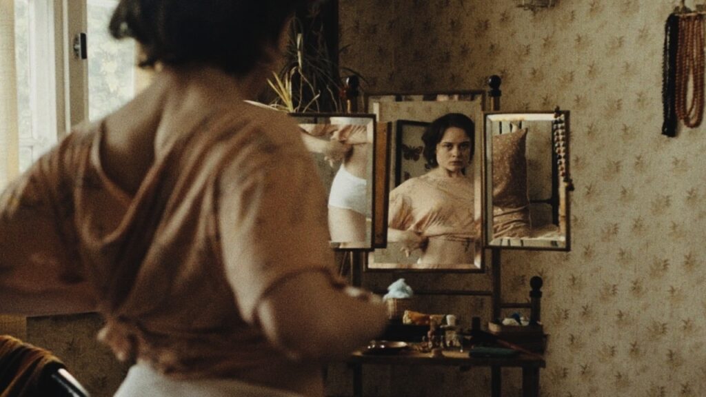 In the 1980s, Angelika examines herself in the mirror