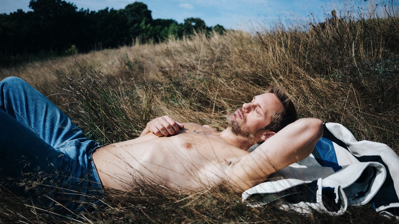A topless Alexander Skarsgård lies in the grass